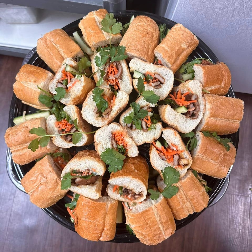 A platter of vPho banh mi sandwiches, cut in half, filled with meat, pickled carrots, and cilantro.