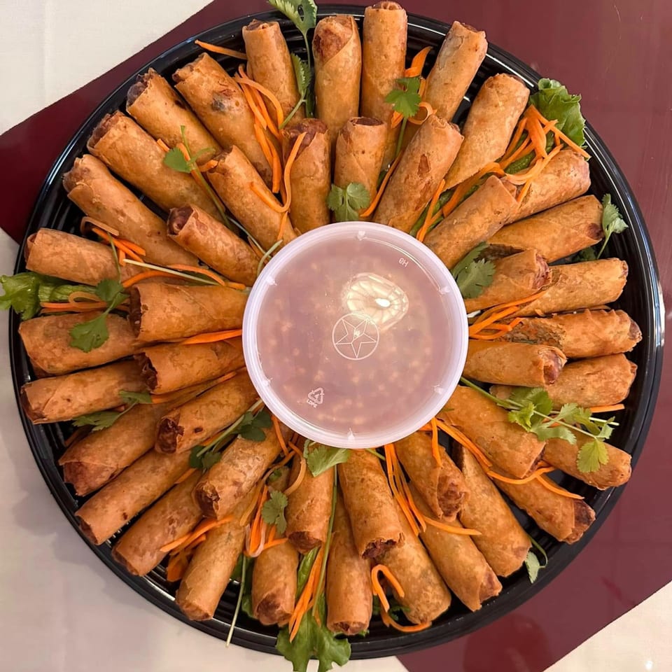 A large platter of vPho's crispy Vietnamese spring rolls arranged around a central dipping sauce.