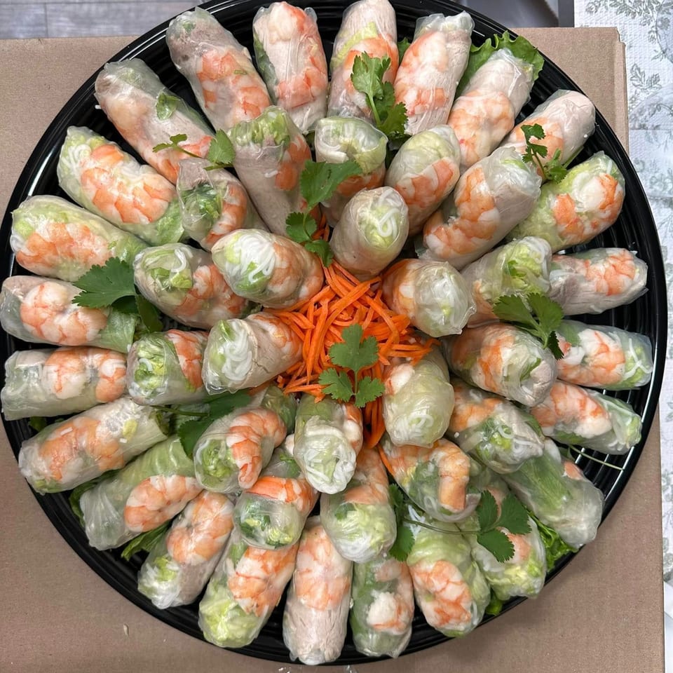 A platter of vPho's Vietnamese spring rolls with shrimp, pork, and vegetables, garnished with cilantro and carrots.