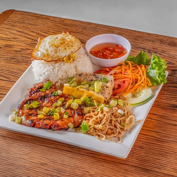 Vietnamese grilled pork, rice, fried egg, egg meatloaf, and pickled vegetables on a white plate.