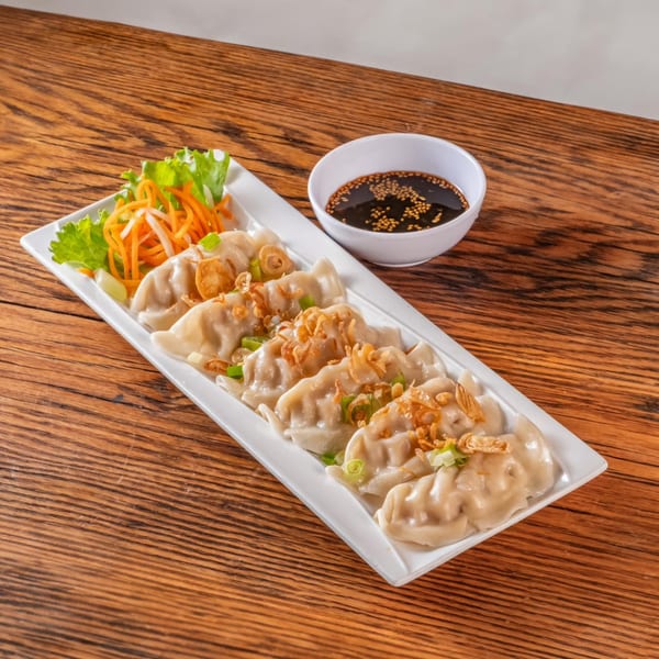 A plate of vPho dumplings with fried onions, green onions, and a side of soy sauce.