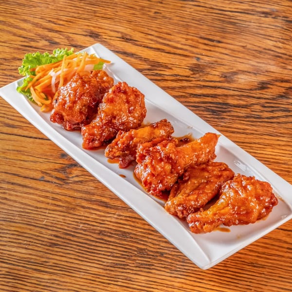 A white rectangular plate of vPho's glazed chicken wings with a side of shredded carrots and lettuce.
