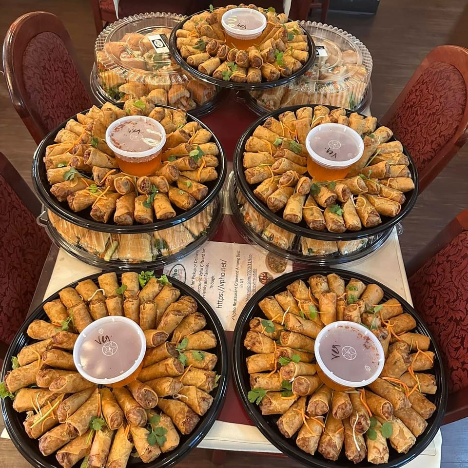 Six large catering trays of vPho's Vietnamese spring rolls and egg rolls with dipping sauces.